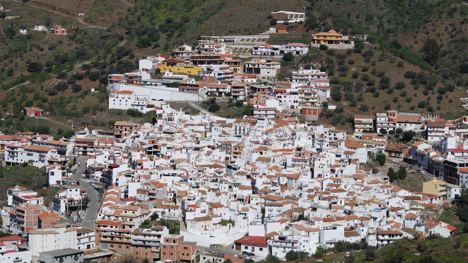 Vista general del pueblo de Arenas, con sus casas blancas escalonadas en la ladera de un monte con olivos y matorral.