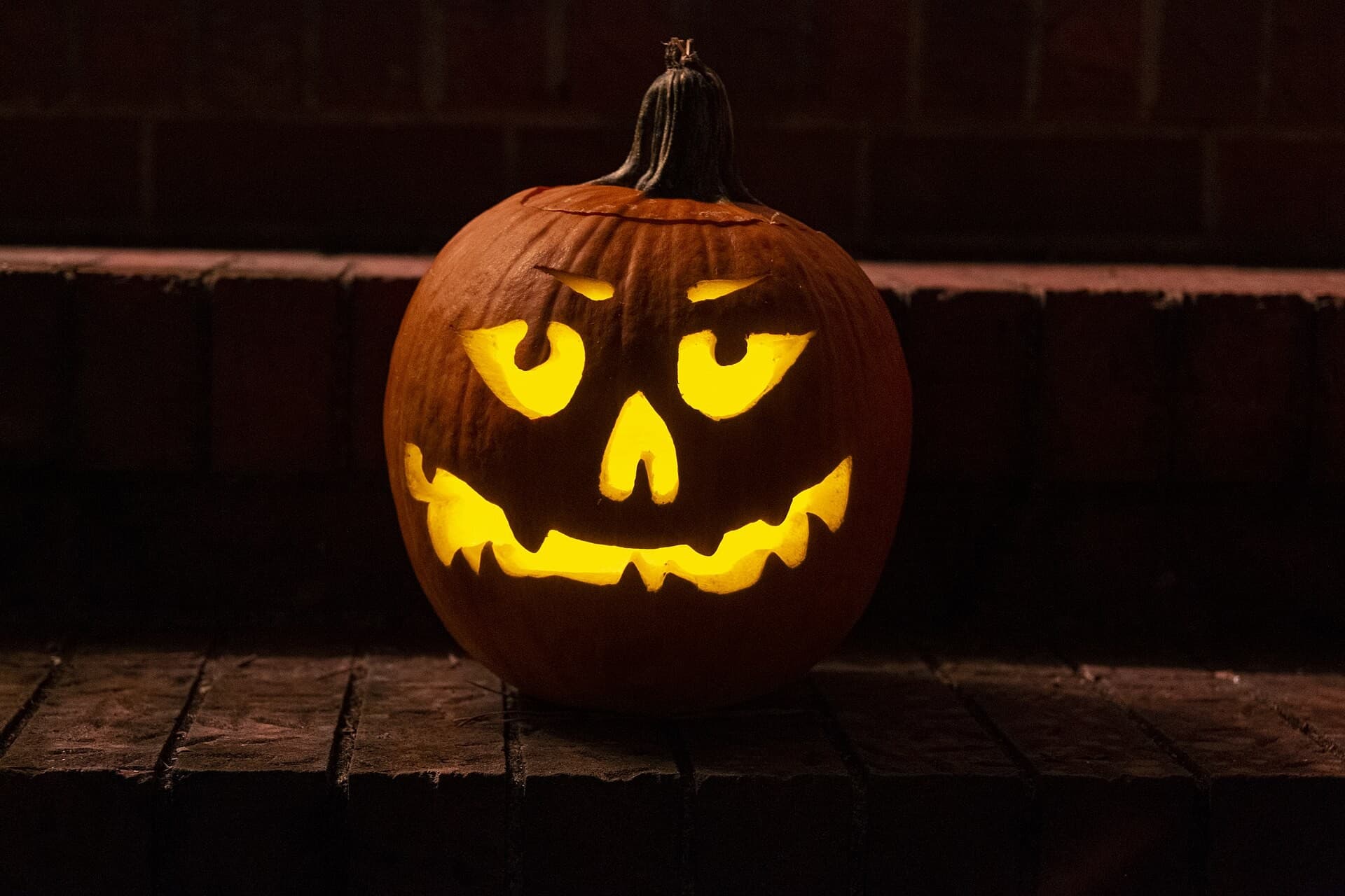 Una calabaza de Halloween tallada con cara sonriente, iluminada por dentro, sobre un escalón de madera en la oscuridad.