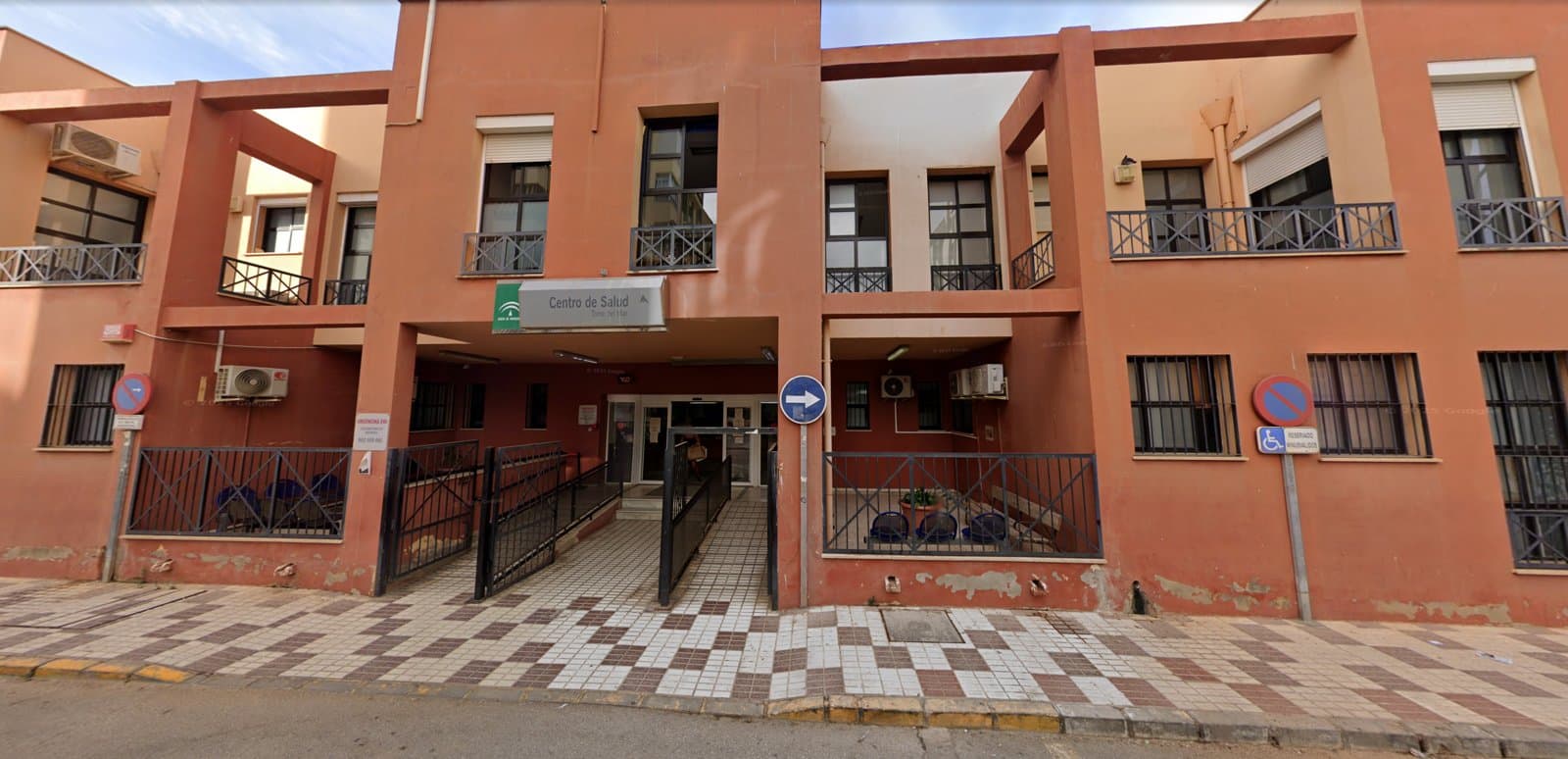 Fachada del Centro de Salud de Torre del Mar, de color teja, con el letrero «Centro de Salud» y el logo de la Junta de Andalucía sobre la entrada, rejas negras y la acera de baldosas.