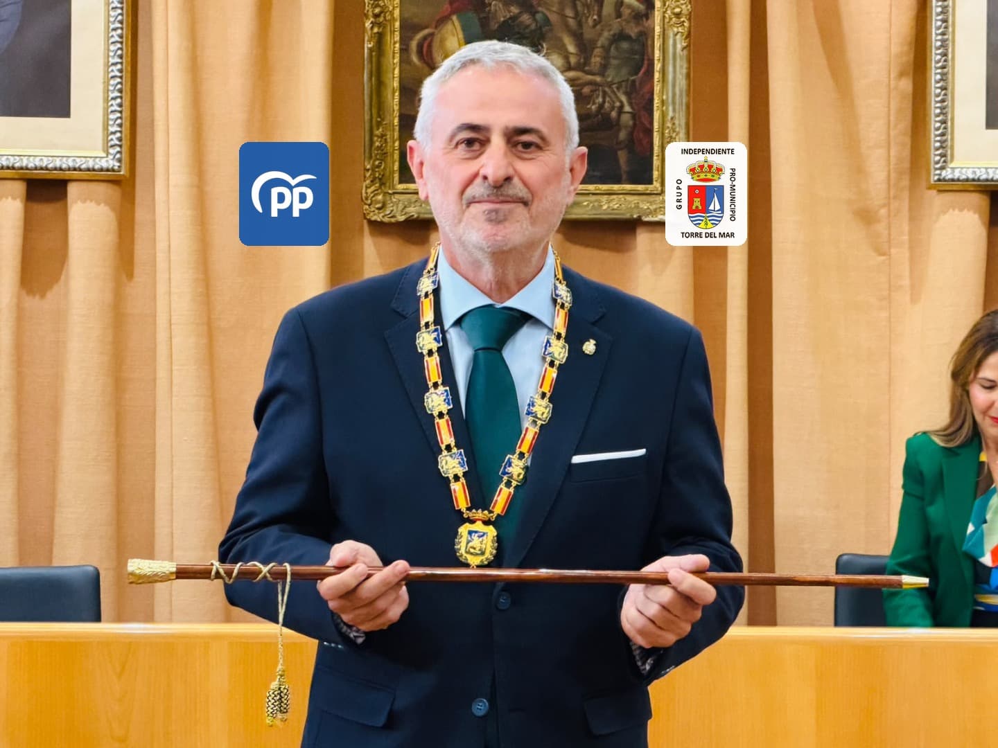 Jesús María Claros, con la medalla de alcalde al cuello, sostiene la vara de mando en el salón de plenos de Vélez-Málaga; a un lado y otro de su cabeza, los logos del Partido Popular y del Grupo Independiente Pro-Municipio de Torre del Mar.