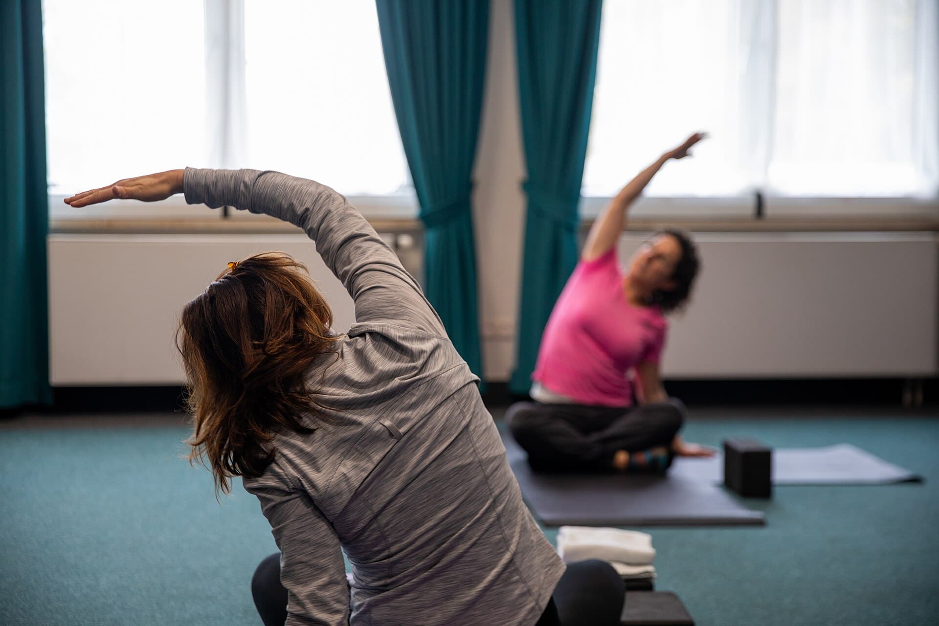Dos mujeres hacen un estiramiento lateral sentadas sobre esterillas en una clase de yoga.