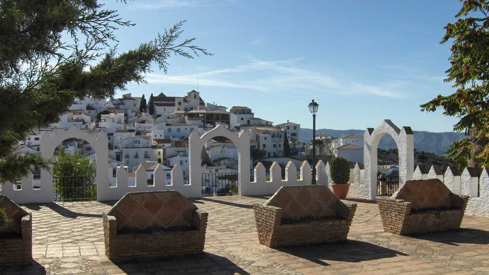 Mirador de Comares con bancos de ladrillo y arcos blancos, y las casas blancas del pueblo al fondo.