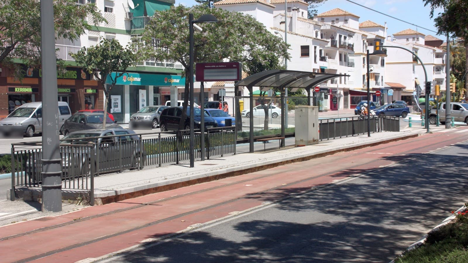 Avenida de Torre del Mar con coches aparcados, una parada con marquesina, árboles y edificios blancos al fondo.