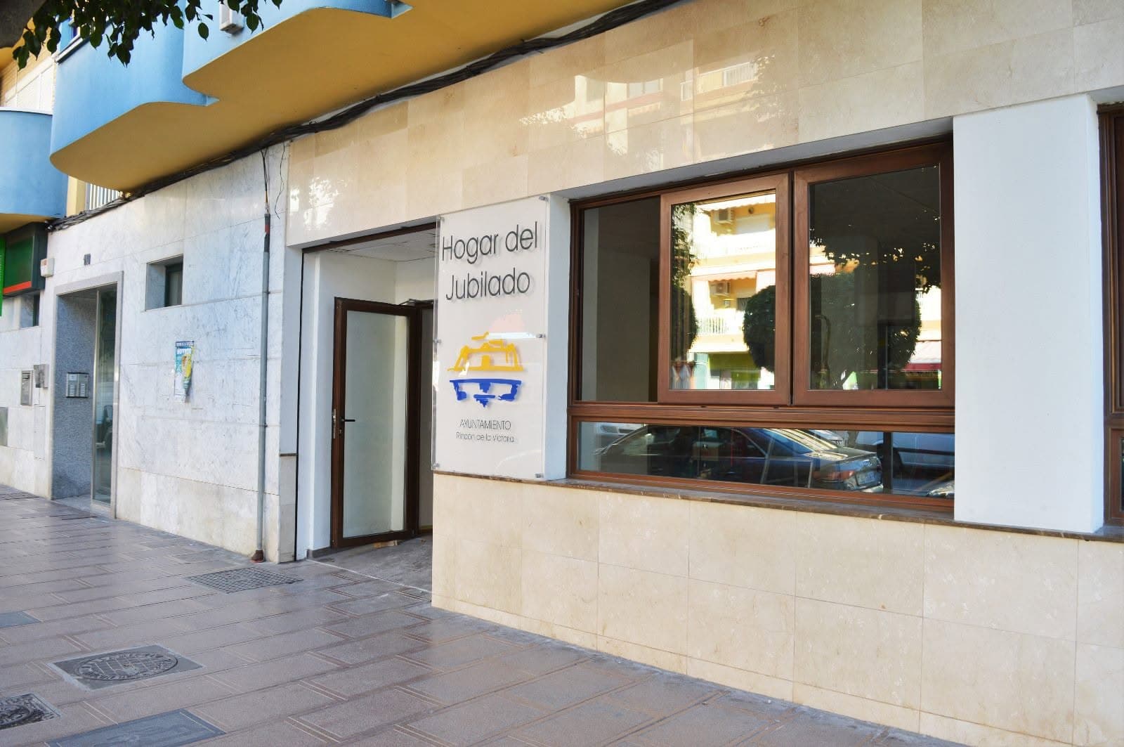 Fachada del Hogar del Jubilado de Rincón de la Victoria, con el cartel del Ayuntamiento junto a la puerta y un gran ventanal.