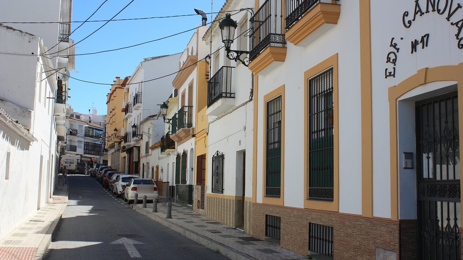 Calle Ingenio, en Nerja: casas blancas con zócalos y balcones de forja, farolas en las fachadas y una fila de coches aparcados a un lado.