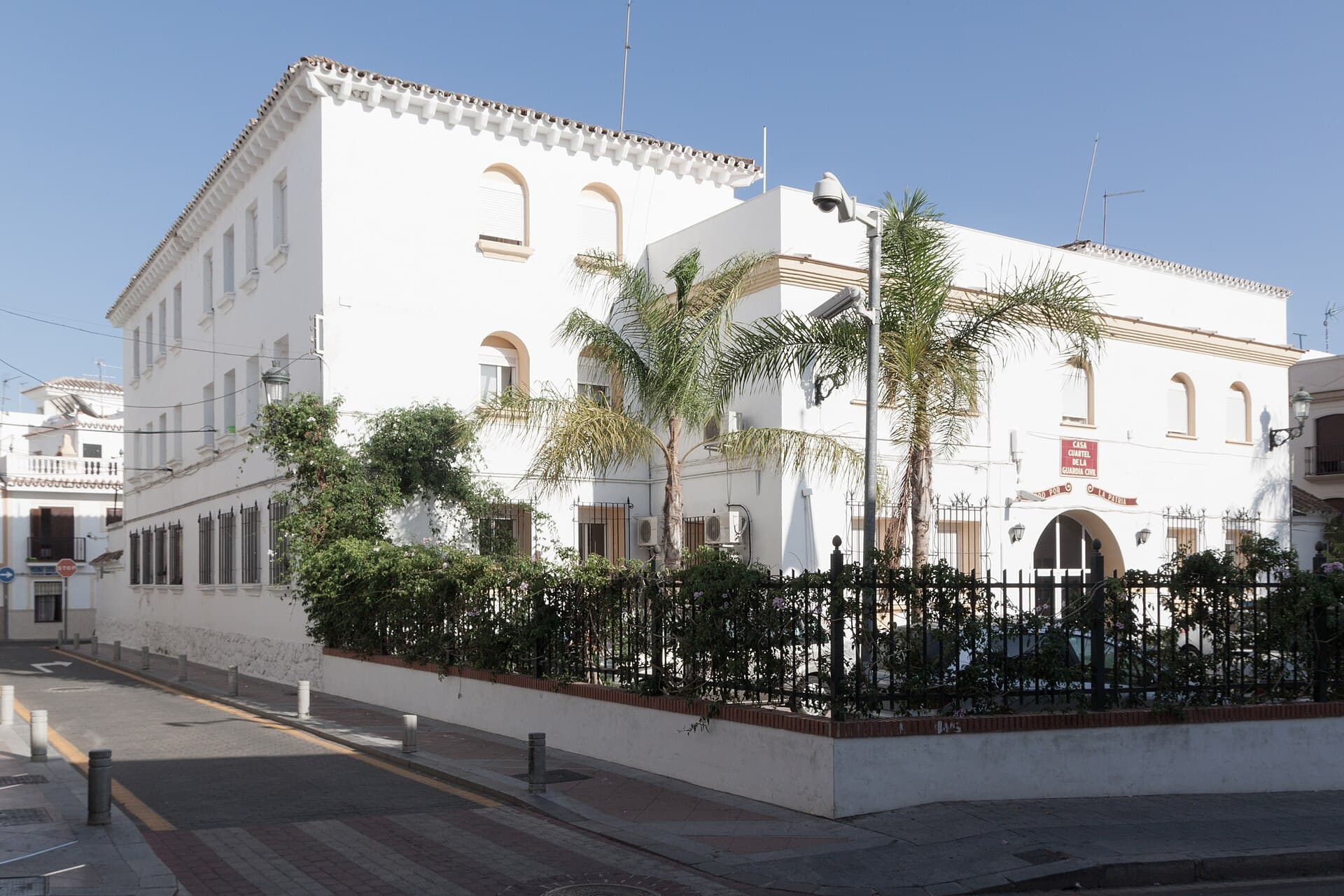 Edificio blanco de la casa cuartel de la Guardia Civil de Nerja, con palmeras y una verja delante