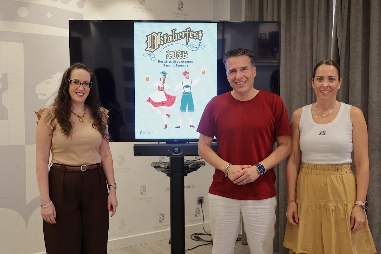 Presentación del Oktoberfest 2026 en el Ayuntamiento de Torrox: el alcalde, Óscar Medina, y dos concejalas junto a una pantalla con el cartel de la fiesta, del 15 al 18 de octubre en el parking Ferrara