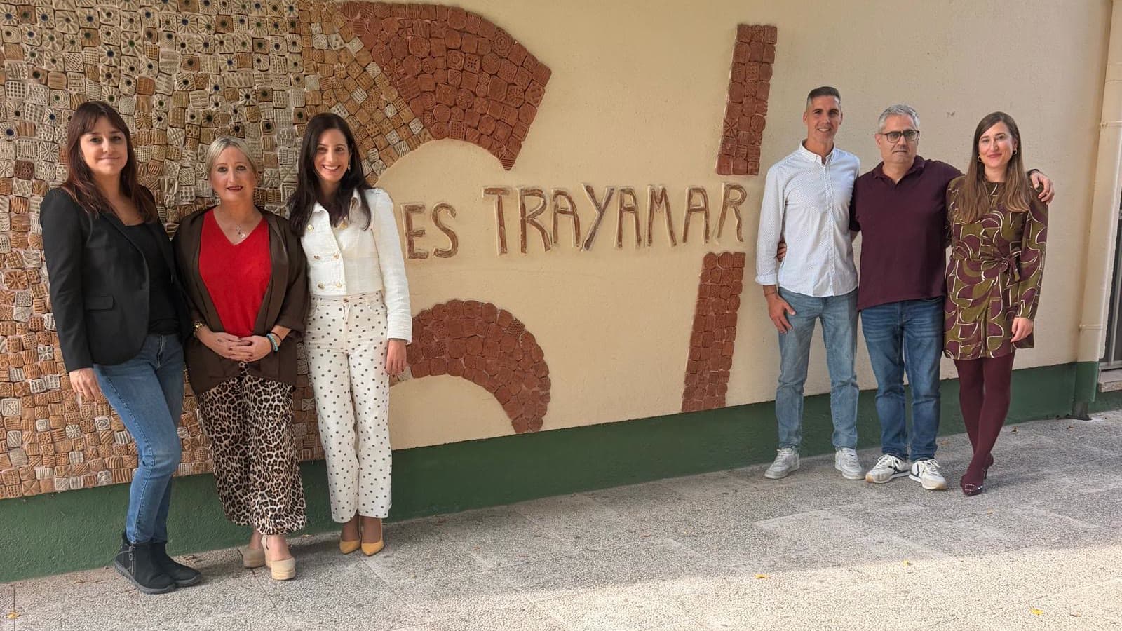 Seis adultos, cuatro mujeres y dos hombres, posan junto a la pared del IES Trayamar, decorada con un mural de piezas de cerámica y el nombre del instituto en letras de barro.