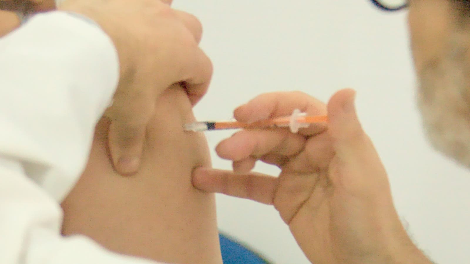 Un sanitario pone una vacuna en el brazo de una persona; en primer plano, la jeringuilla