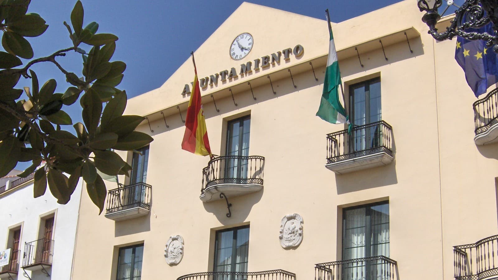 Fachada del Ayuntamiento de Vélez-Málaga, con el rótulo «Ayuntamiento», el reloj, balcones de forja y las banderas de España, Andalucía y la Unión Europea.