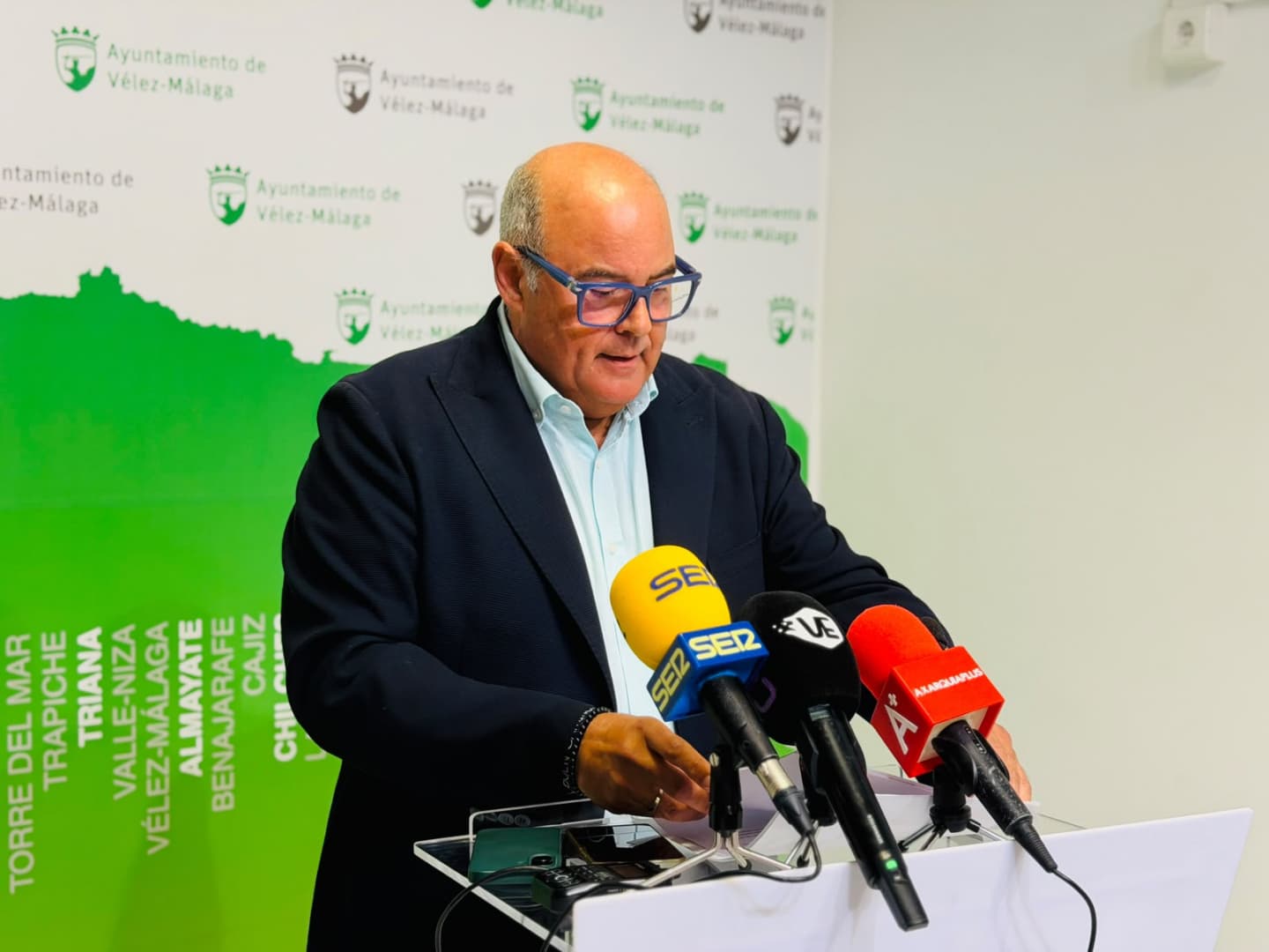 Jesús Lupiáñez, con americana azul y gafas, habla ante varios micrófonos en la sala de prensa del Ayuntamiento de Vélez-Málaga