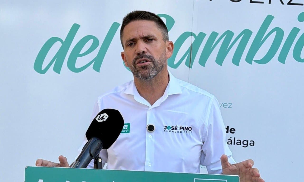 José Pino, con camisa blanca de su candidatura, habla ante un micrófono en un atril de Andalucía Por Sí, con un cartel verde detrás.