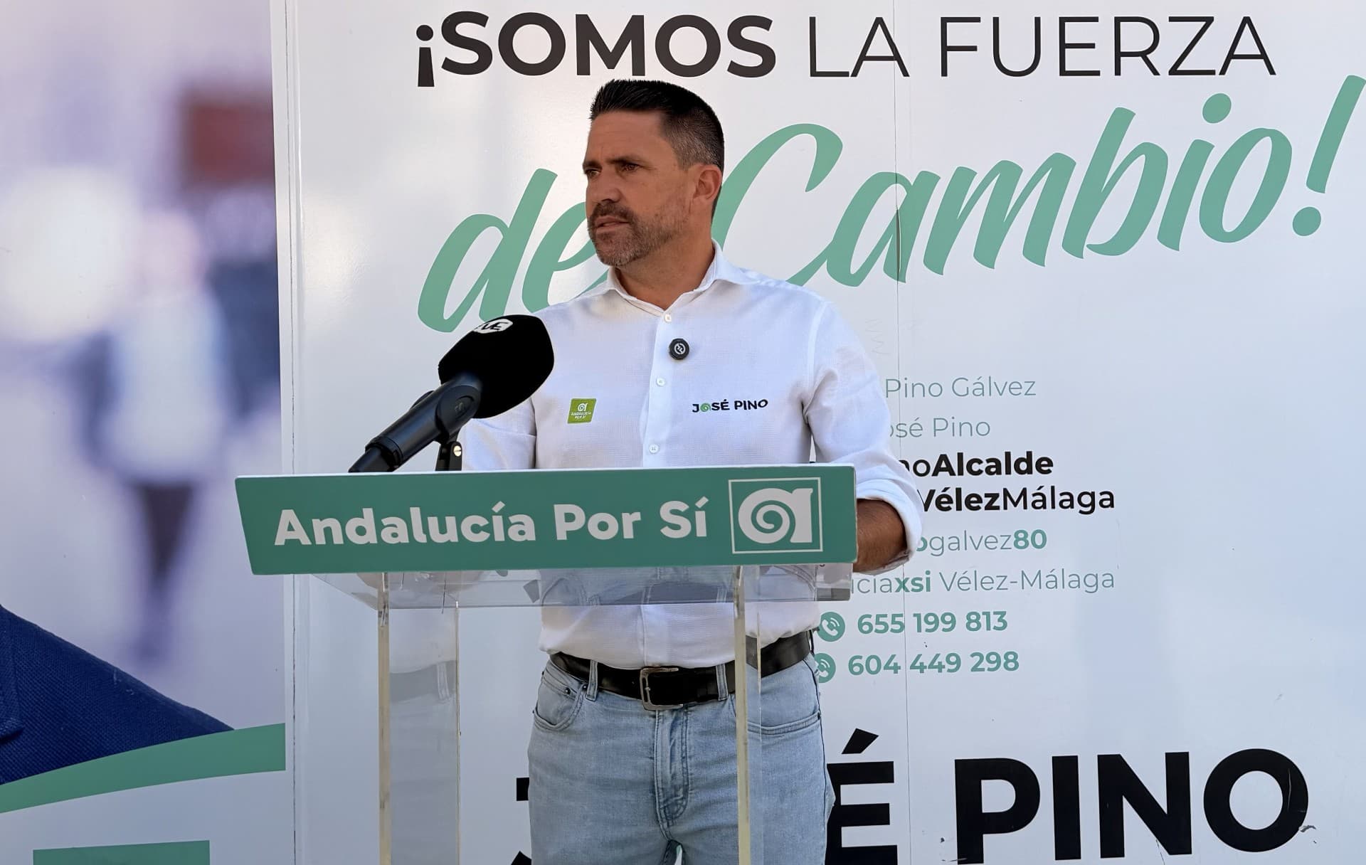 José Pino, con camisa blanca, habla ante un atril de Andalucía Por Sí y un micrófono, delante de un cartel del partido