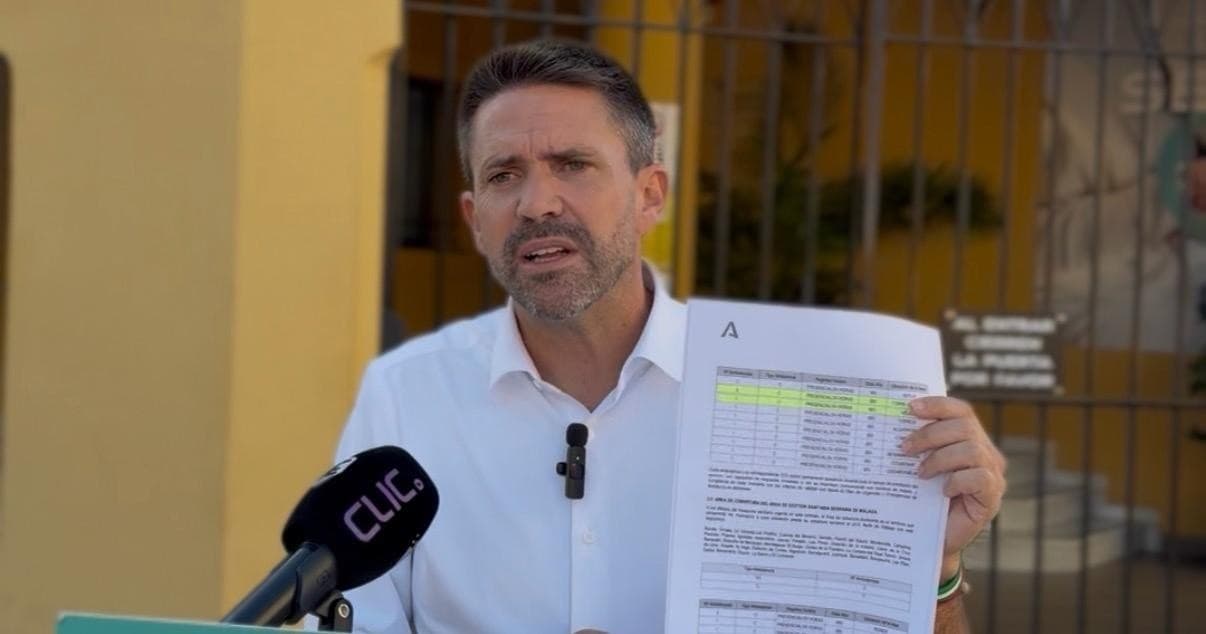 José Pino, portavoz de Andalucía Por Sí, enseña a la cámara el pliego del contrato de las ambulancias de la Junta mientras habla ante un micrófono, junto a una reja, en Vélez-Málaga.