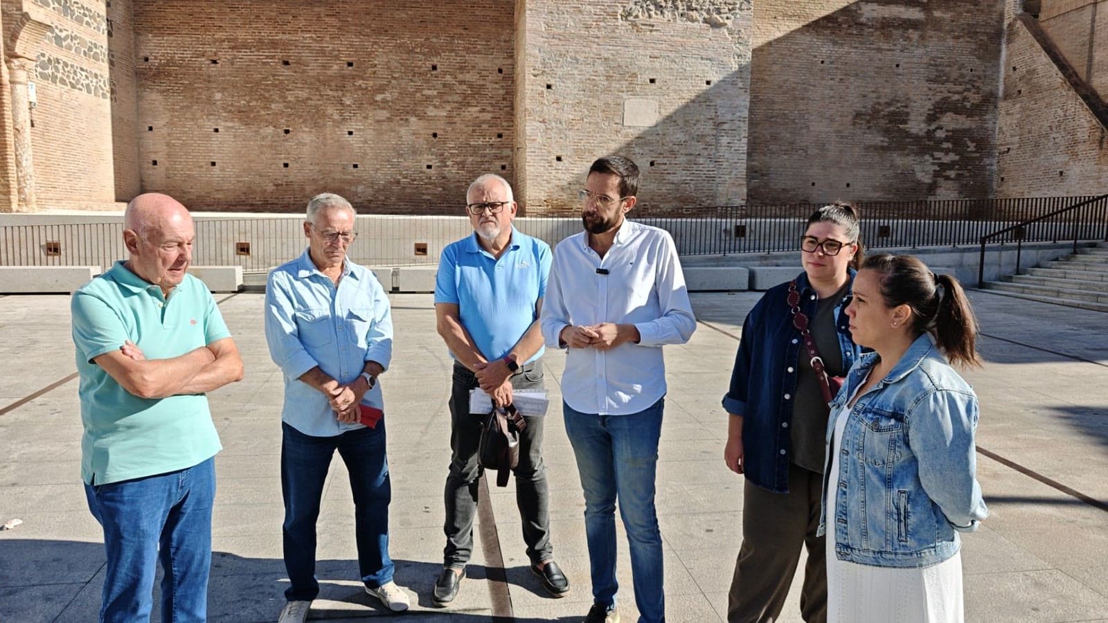Víctor González, portavoz del PSOE de Vélez-Málaga, habla con otros cinco miembros del partido en una plaza, delante de un muro de ladrillo antiguo.