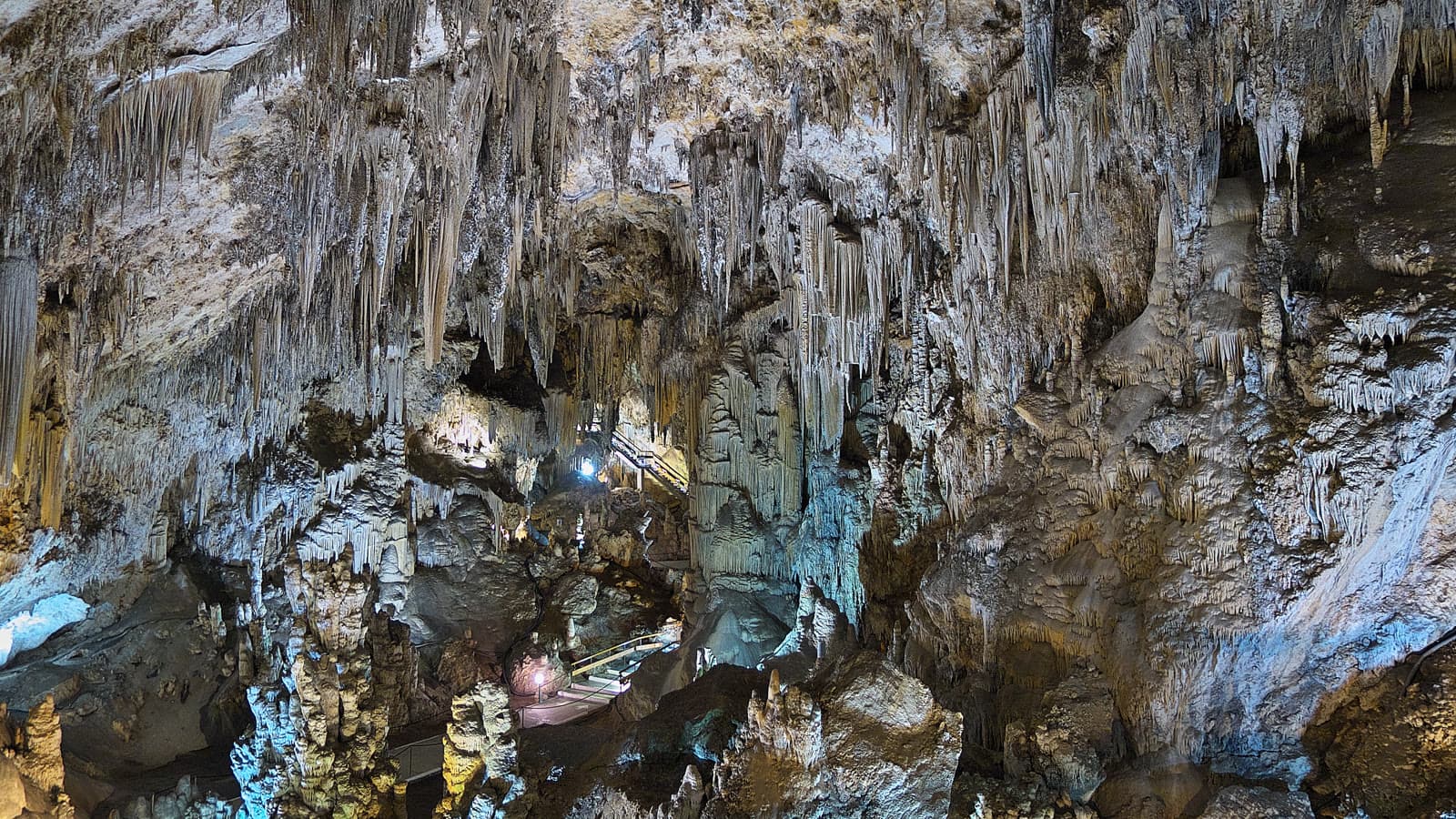 Interior de la Cueva de Nerja con estalactitas y columnas iluminadas y, al fondo, las pasarelas y escaleras del recorrido turístico.