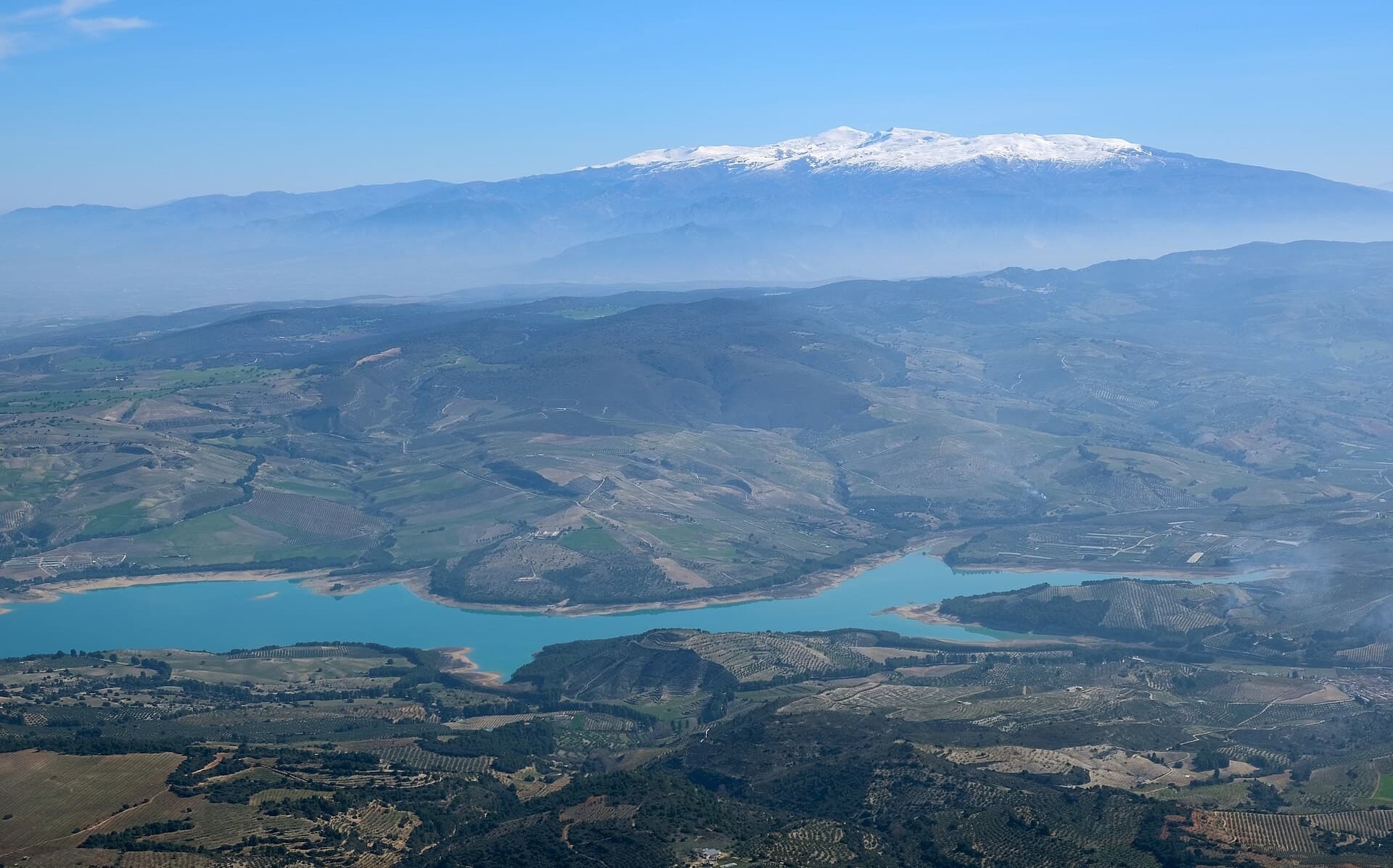 Vista aérea del embalse de La Viñuela entre las lomas de la Axarquía, con Sierra Nevada nevada al fondo.