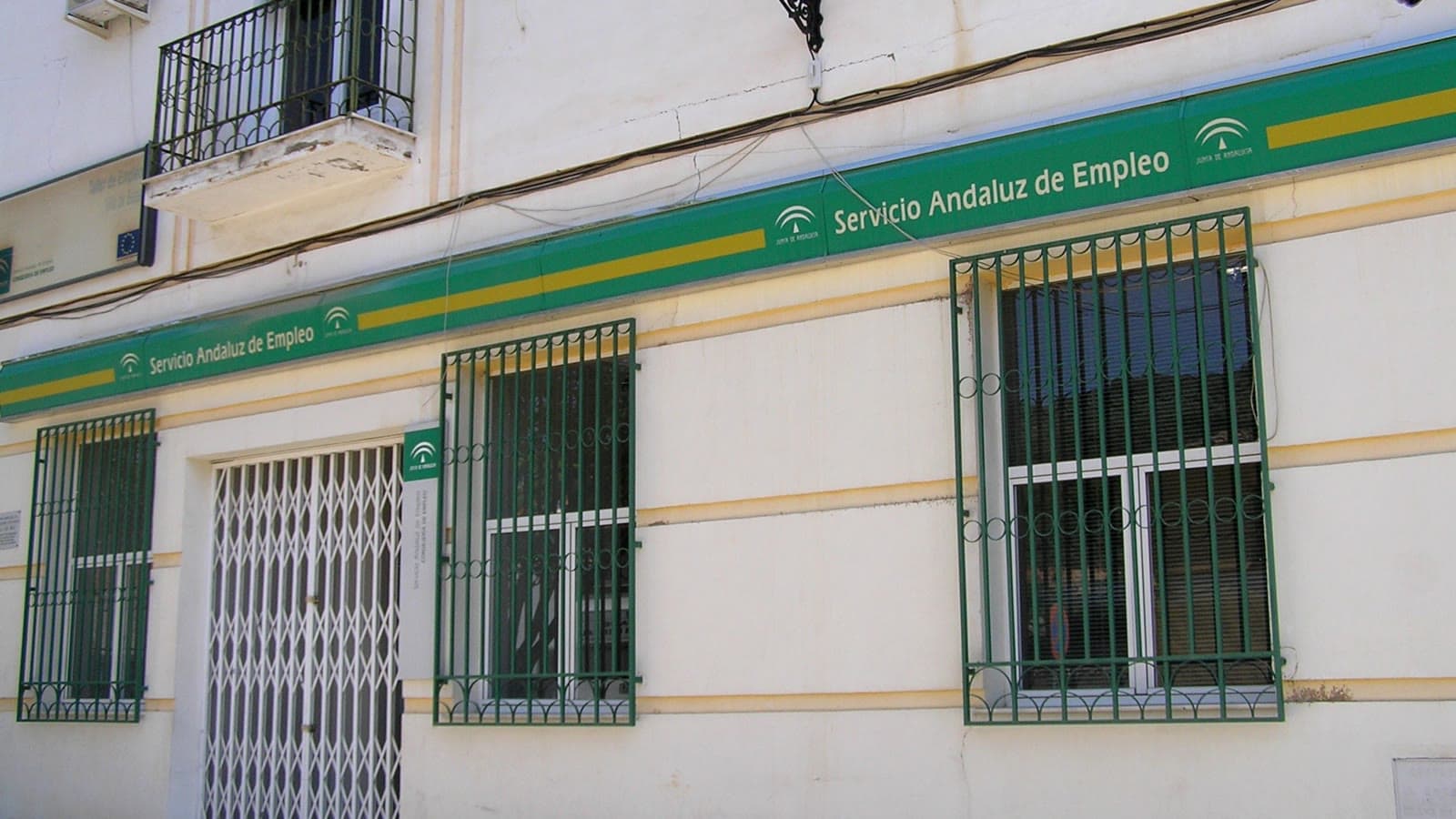 Fachada de una oficina del Servicio Andaluz de Empleo, con el rótulo verde y blanco de la Junta de Andalucía sobre las ventanas enrejadas y la puerta de entrada.