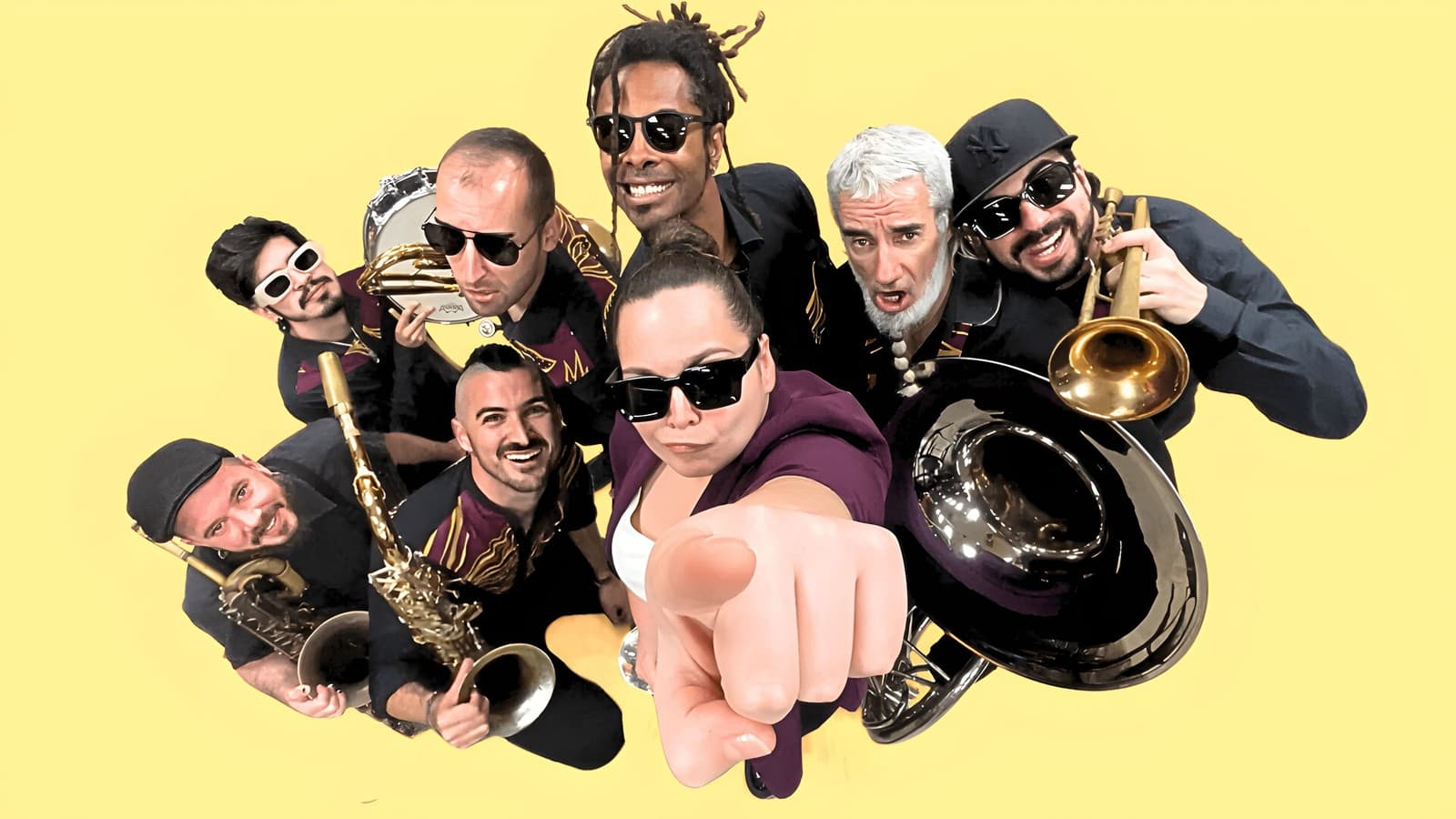Los músicos de la Gata Brass Band, con sus instrumentos de viento, fotografiados desde arriba sobre un fondo amarillo.