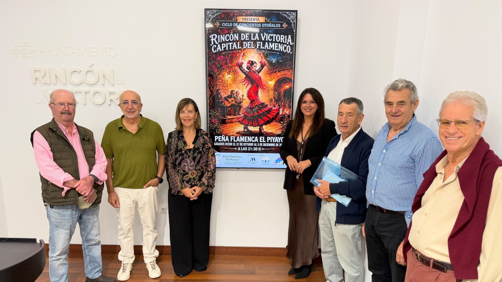 Siete personas posan en una sala del Ayuntamiento de Rincón de la Victoria a ambos lados de una pantalla con el cartel del ciclo «Rincón de la Victoria, capital del Flamenco», en el que aparece una bailaora con traje rojo de volantes y, abajo, «Peña Flamenca El Piyayo, sábados desde el 31 de octubre al 5 de diciembre, a las 21:30 h».