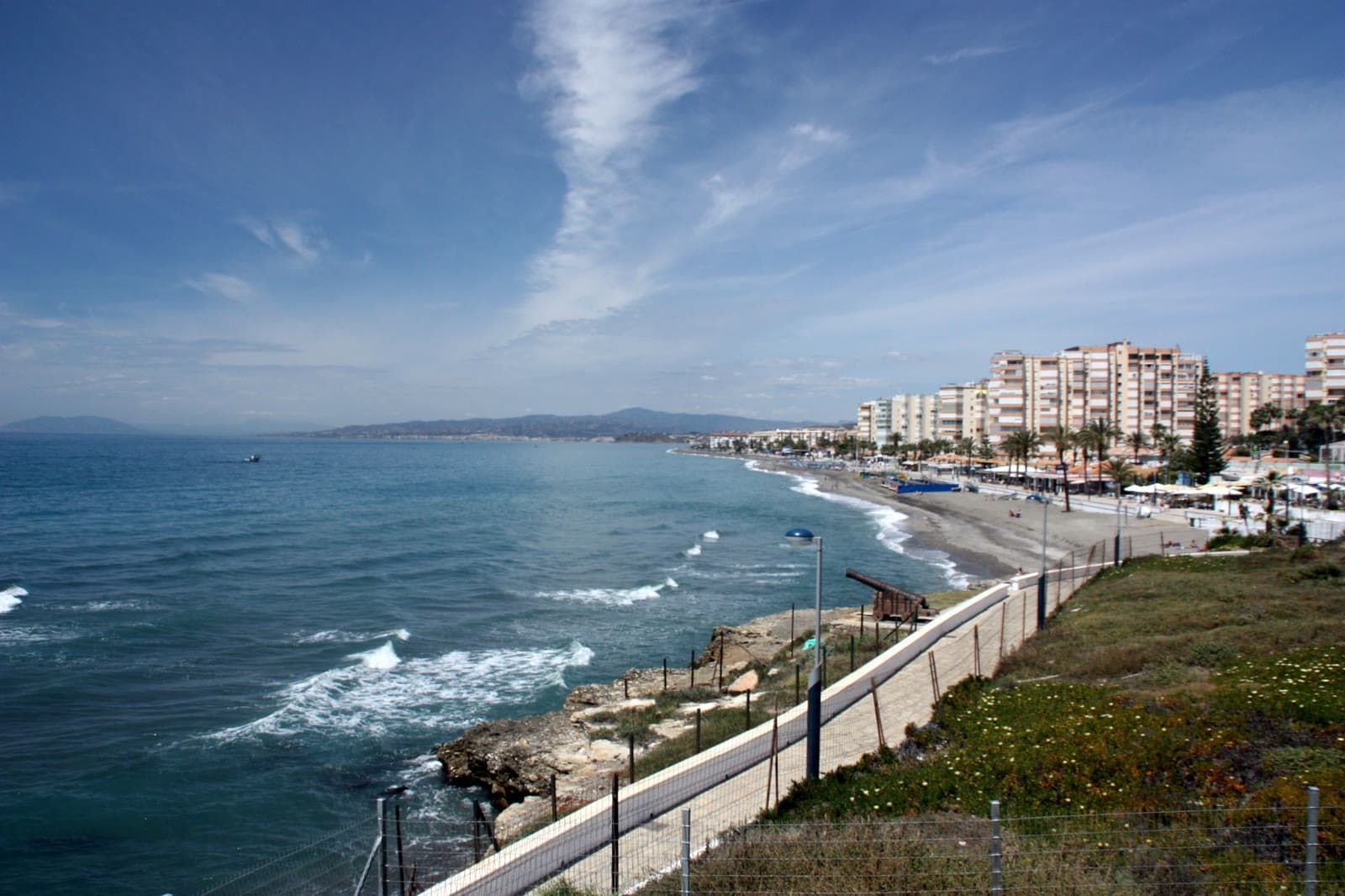 Vista de Torrox Costa desde el faro: la playa, el paseo marítimo con palmeras y la línea de edificios junto al mar