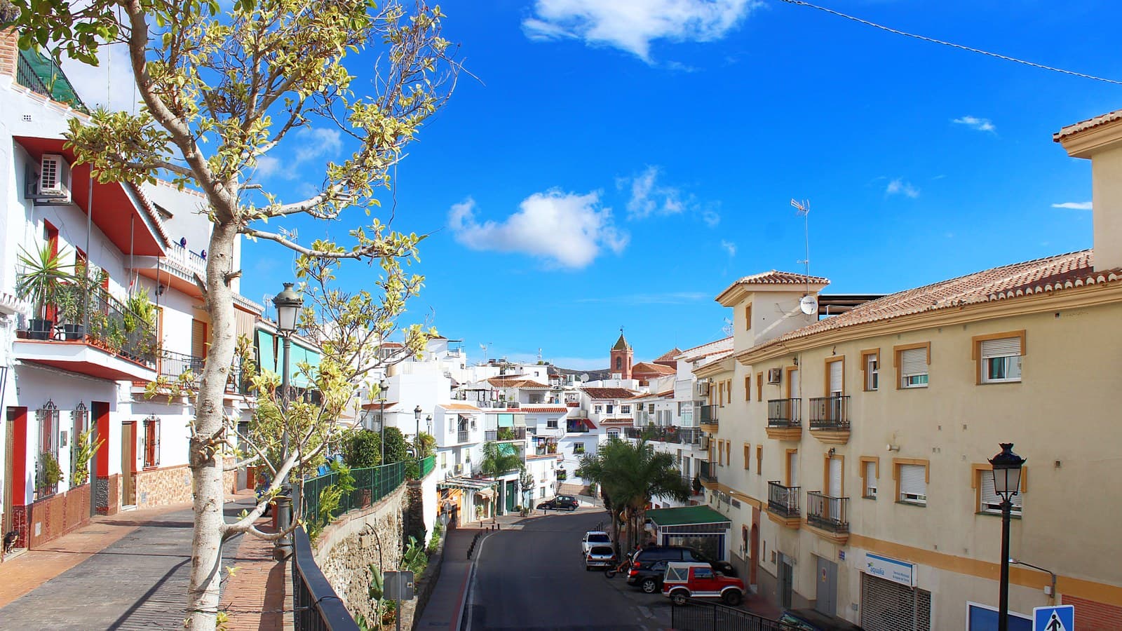 Calle de Torrox pueblo con casas blancas y edificios de color crema, y la torre de la iglesia al fondo.